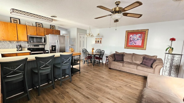 kitchen with a breakfast bar area, stainless steel appliances, backsplash, ceiling fan with notable chandelier, and dark hardwood / wood-style flooring