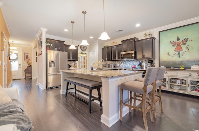 kitchen with an island with sink, a breakfast bar, dark brown cabinetry, pendant lighting, and appliances with stainless steel finishes