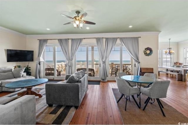 living room with ornamental molding, a wealth of natural light, ceiling fan with notable chandelier, and hardwood / wood-style floors