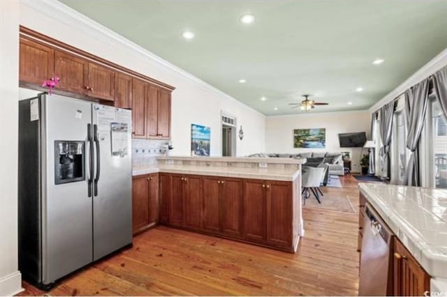 kitchen featuring kitchen peninsula, ceiling fan, appliances with stainless steel finishes, light hardwood / wood-style floors, and tile counters