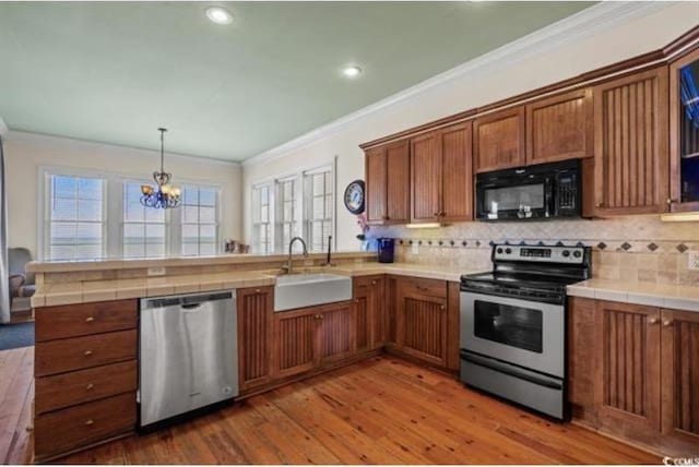 kitchen with tile counters, stainless steel appliances, wood-type flooring, sink, and crown molding