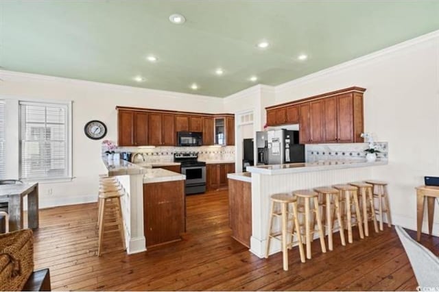 kitchen with kitchen peninsula, decorative backsplash, appliances with stainless steel finishes, a kitchen bar, and dark hardwood / wood-style floors