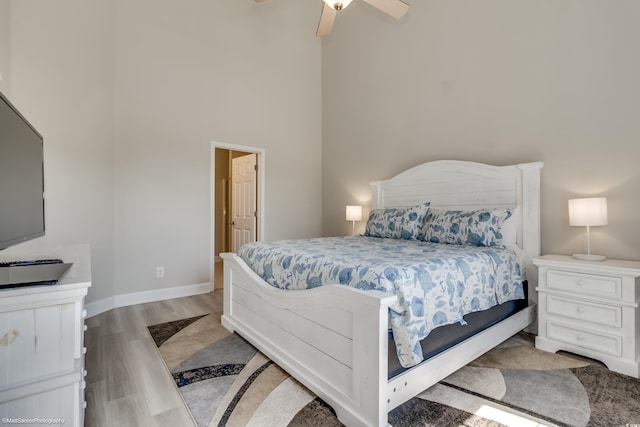 bedroom with a towering ceiling, light wood-type flooring, and ceiling fan