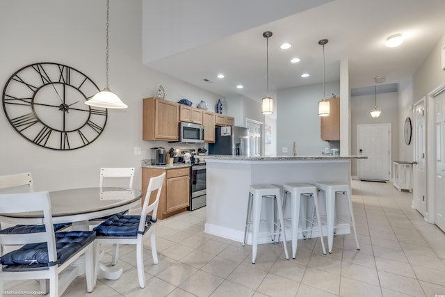 kitchen with a breakfast bar, decorative light fixtures, light tile patterned floors, appliances with stainless steel finishes, and light stone counters