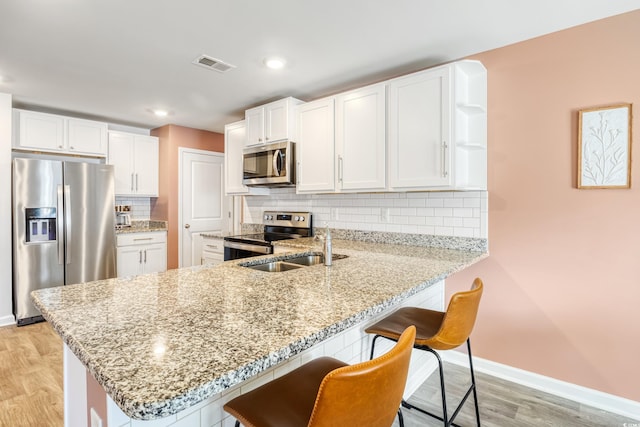 kitchen featuring kitchen peninsula, white cabinets, light wood-type flooring, and appliances with stainless steel finishes