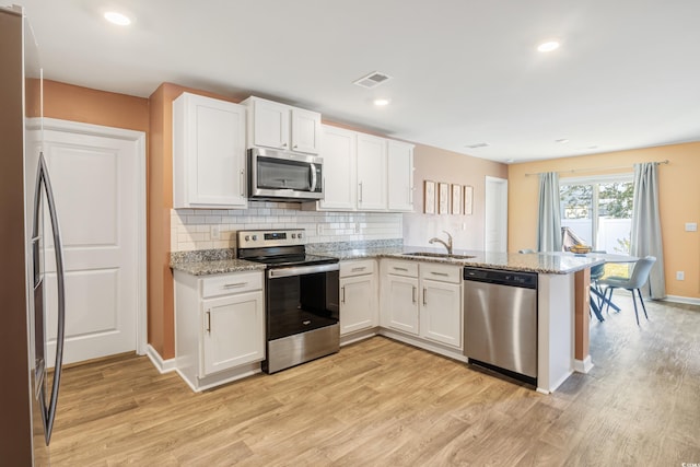 kitchen with stainless steel appliances, white cabinets, kitchen peninsula, light stone countertops, and light wood-type flooring