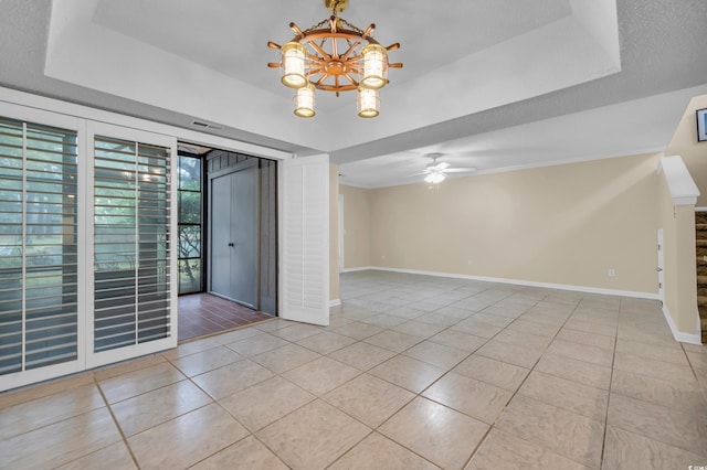 tiled empty room with ceiling fan with notable chandelier and a raised ceiling