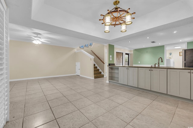 unfurnished living room featuring a raised ceiling, sink, light tile patterned floors, and ceiling fan with notable chandelier