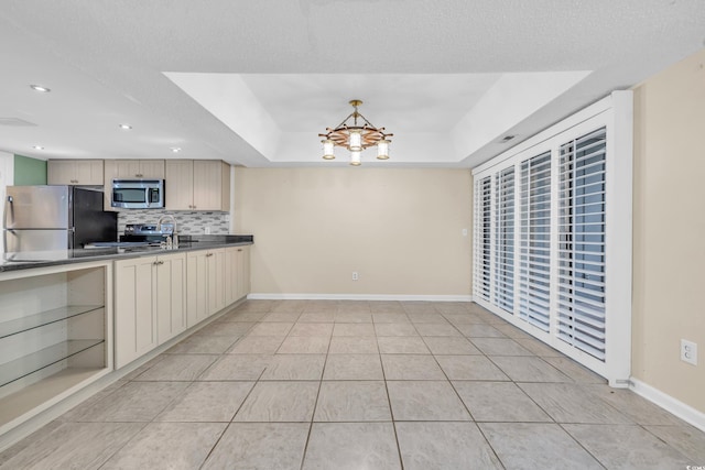 kitchen with stainless steel appliances, an inviting chandelier, backsplash, a tray ceiling, and light tile patterned floors