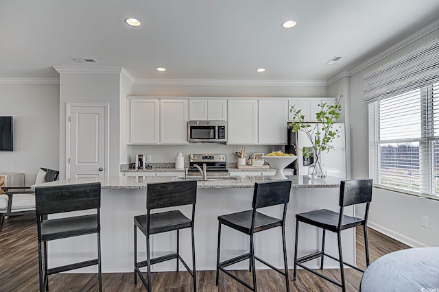 kitchen with white cabinetry, dark hardwood / wood-style floors, appliances with stainless steel finishes, and a center island with sink