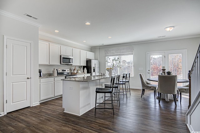 kitchen with ornamental molding, an island with sink, stainless steel appliances, and white cabinetry