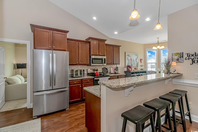 kitchen with light stone counters, stainless steel appliances, pendant lighting, vaulted ceiling, and a breakfast bar area