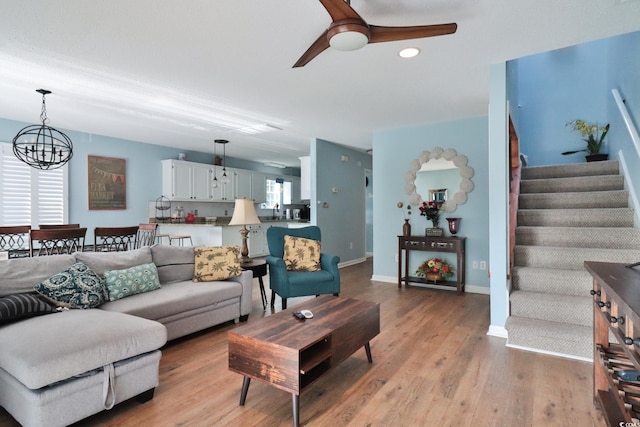 living room with ceiling fan with notable chandelier and light hardwood / wood-style flooring