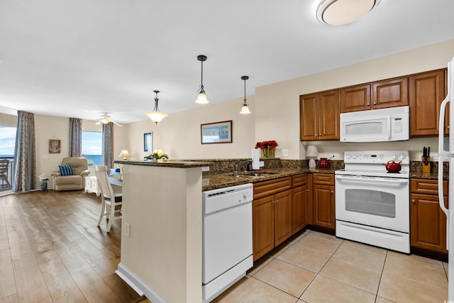 kitchen with dark stone countertops, pendant lighting, light hardwood / wood-style floors, sink, and white appliances