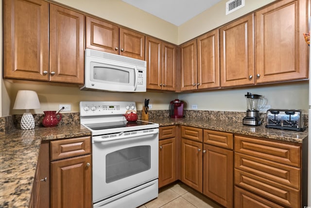 kitchen featuring light tile patterned flooring, dark stone counters, and white appliances