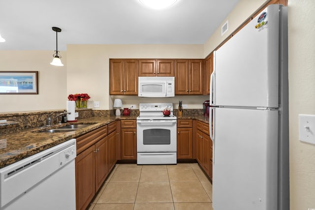 kitchen with hanging light fixtures, light tile patterned floors, dark stone counters, sink, and white appliances