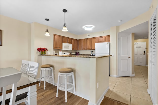 kitchen featuring kitchen peninsula, decorative light fixtures, light wood-type flooring, stone counters, and white appliances