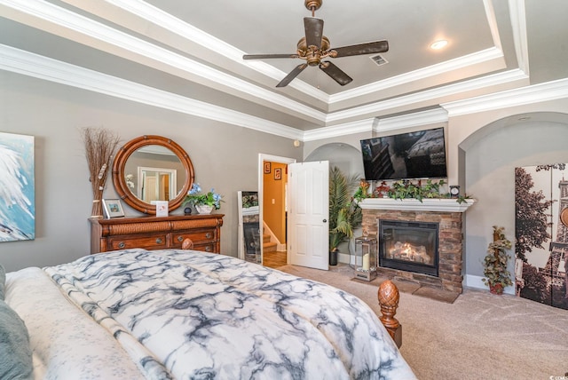 carpeted bedroom with crown molding, a fireplace, a tray ceiling, and ceiling fan