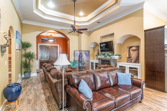 living room featuring crown molding, light wood-type flooring, a fireplace, and ceiling fan