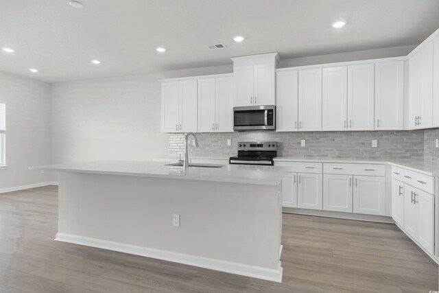 kitchen with white cabinetry, sink, an island with sink, appliances with stainless steel finishes, and light wood-type flooring