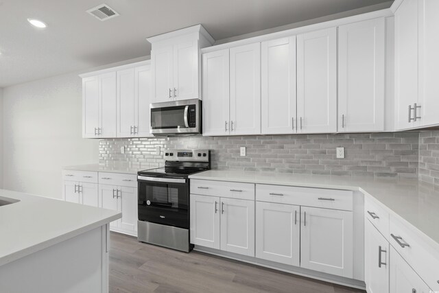 kitchen with white cabinets, light wood-type flooring, appliances with stainless steel finishes, and tasteful backsplash