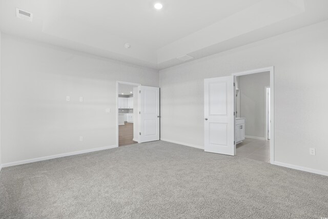 unfurnished bedroom with a raised ceiling, light colored carpet, and connected bathroom