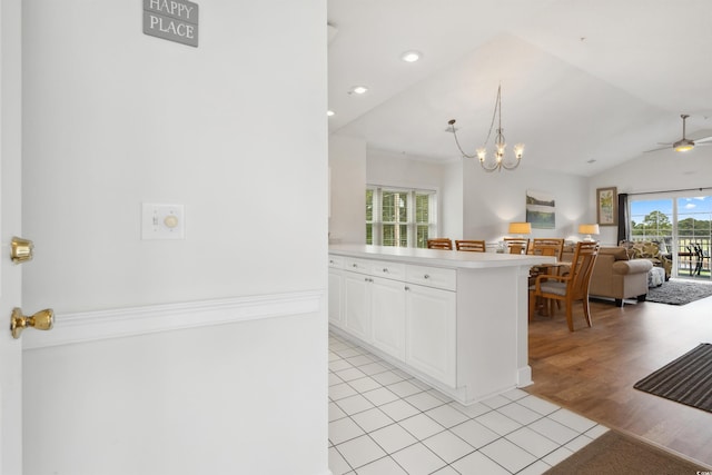 kitchen with lofted ceiling, white cabinets, light wood-type flooring, ceiling fan with notable chandelier, and decorative light fixtures