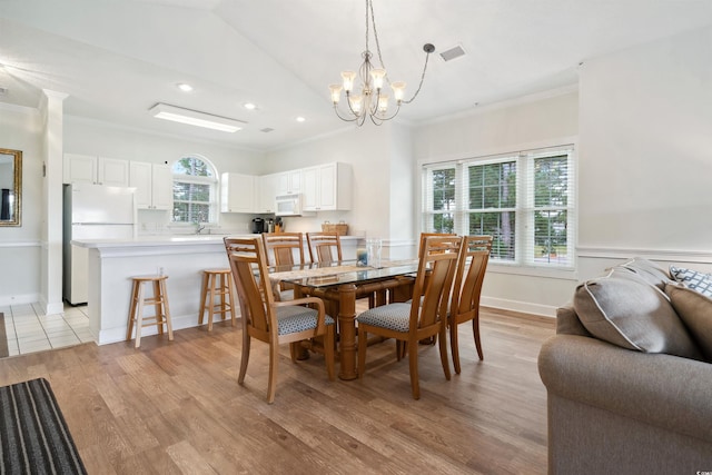 dining area with light wood-type flooring, a notable chandelier, ornamental molding, and plenty of natural light