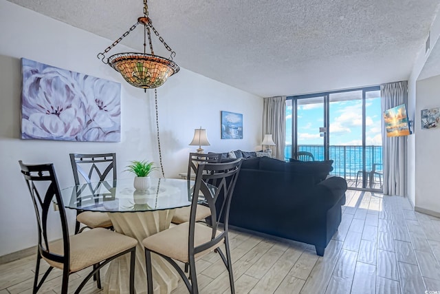 dining area with a water view, expansive windows, a textured ceiling, and light wood-type flooring