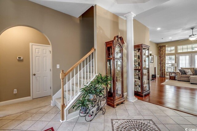 entryway featuring ceiling fan, arched walkways, light tile patterned floors, baseboards, and stairs