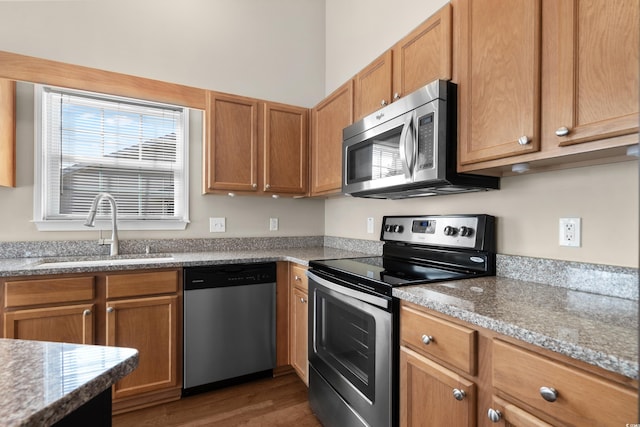 kitchen featuring stainless steel appliances, a sink, light stone countertops, brown cabinetry, and dark wood finished floors