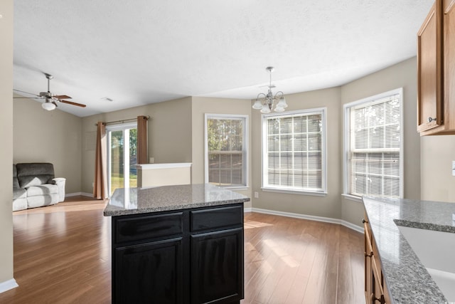 kitchen with open floor plan, dark cabinetry, light stone counters, and a center island