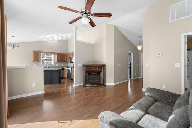 living area with visible vents, a glass covered fireplace, lofted ceiling, dark wood-style flooring, and ceiling fan with notable chandelier