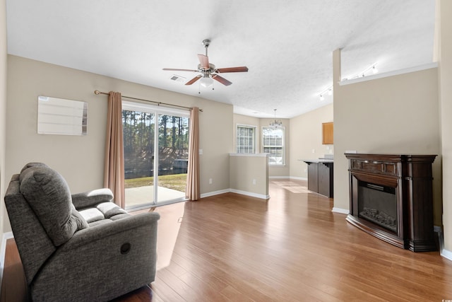 living room with baseboards, a glass covered fireplace, ceiling fan, a textured ceiling, and light wood-type flooring