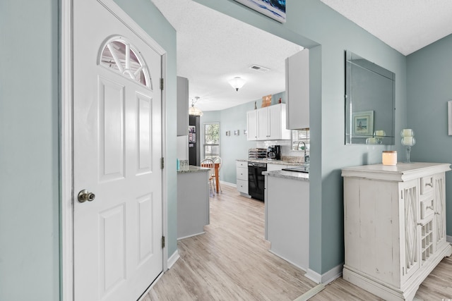 kitchen featuring light wood finished floors, black dishwasher, visible vents, white cabinets, and a textured ceiling