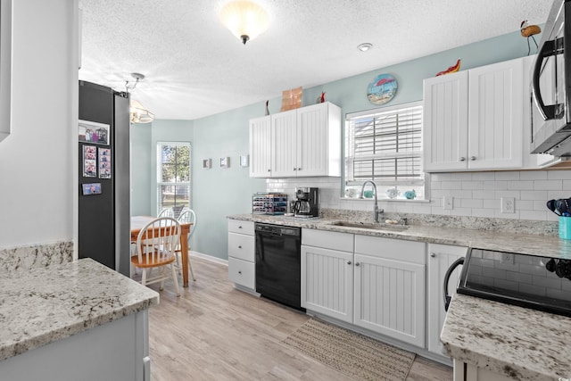 kitchen featuring black dishwasher, light wood finished floors, tasteful backsplash, a sink, and a textured ceiling