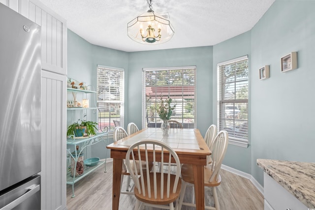 dining space with light wood finished floors, a textured ceiling, and an inviting chandelier