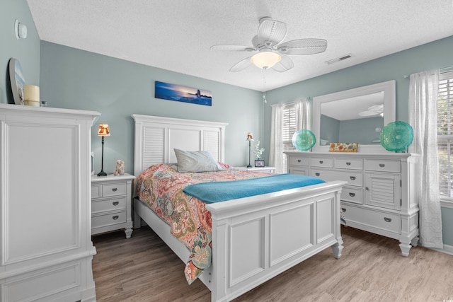 bedroom featuring light wood-style floors, ceiling fan, multiple windows, and visible vents