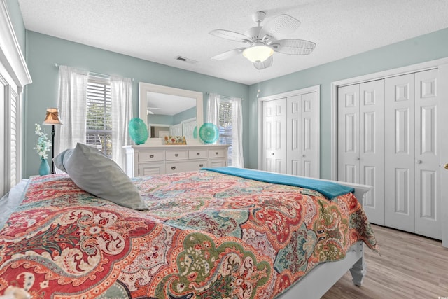 bedroom with a textured ceiling, ceiling fan, visible vents, light wood-style floors, and two closets