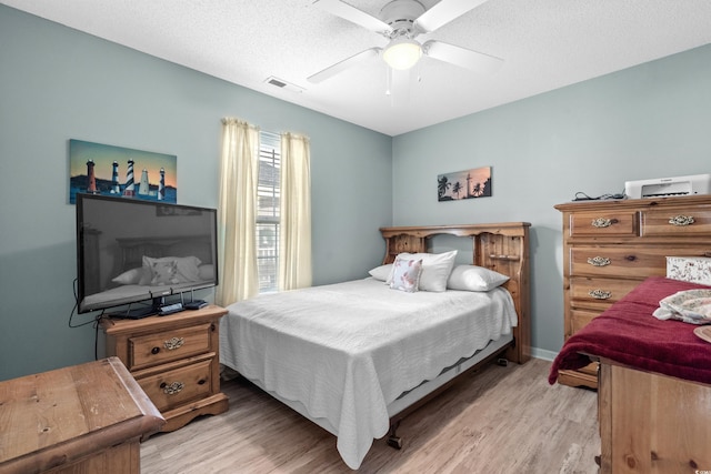 bedroom with a textured ceiling, ceiling fan, visible vents, and light wood-style floors