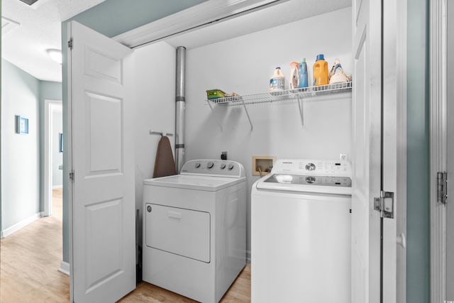 washroom with light wood-type flooring, laundry area, baseboards, and washer and clothes dryer