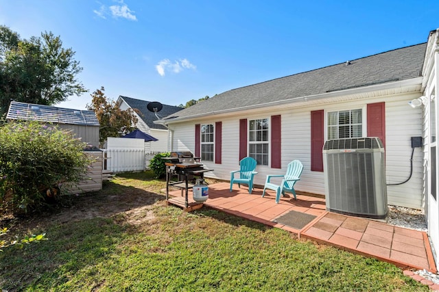 rear view of property featuring a shingled roof, fence, a yard, central air condition unit, and a patio area