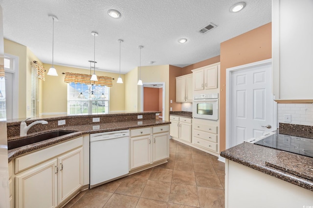 kitchen with dark stone counters, a textured ceiling, backsplash, white appliances, and pendant lighting