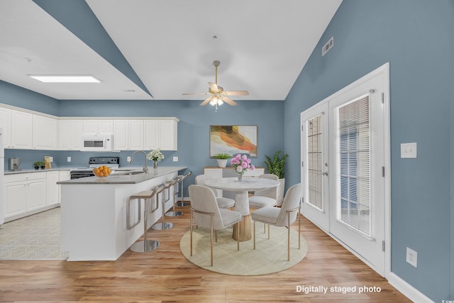 kitchen featuring white appliances, light hardwood / wood-style floors, white cabinetry, and a center island with sink