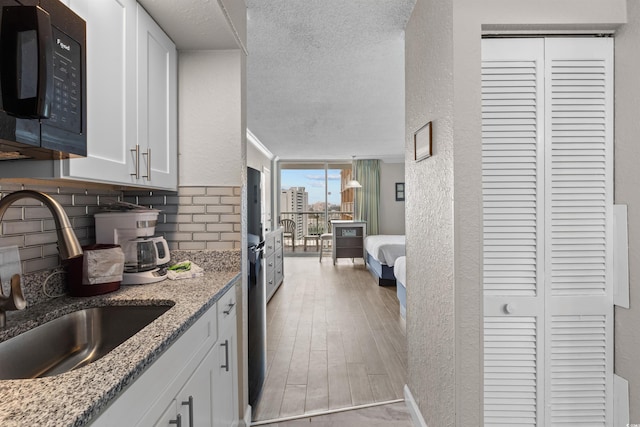 9550 Shore Dr Unit 1202, Myrtle Beach, SC 29572 - kitchen featuring black microwave, a sink, tasteful backsplash, white cabinets, and a textured ceiling