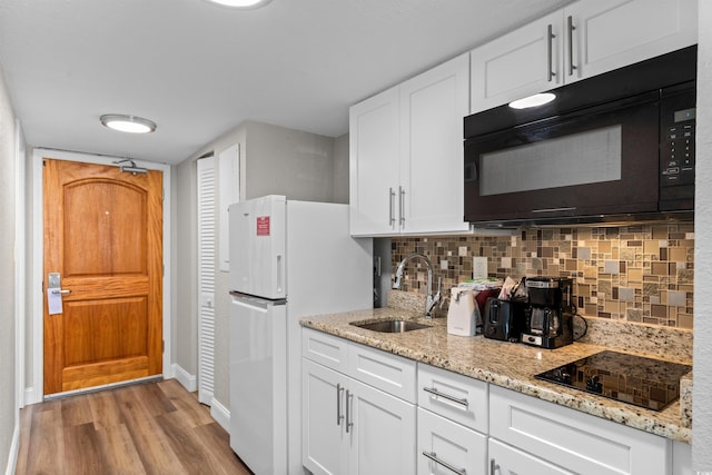 kitchen with decorative backsplash, white cabinetry, light wood-type flooring, black appliances, and sink