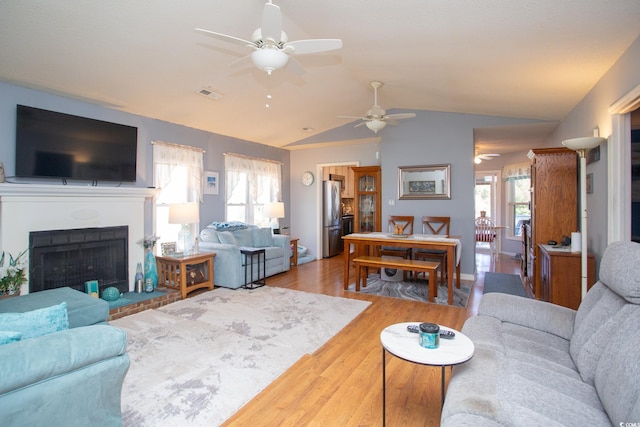 living room featuring a wealth of natural light, lofted ceiling, light hardwood / wood-style flooring, and a fireplace