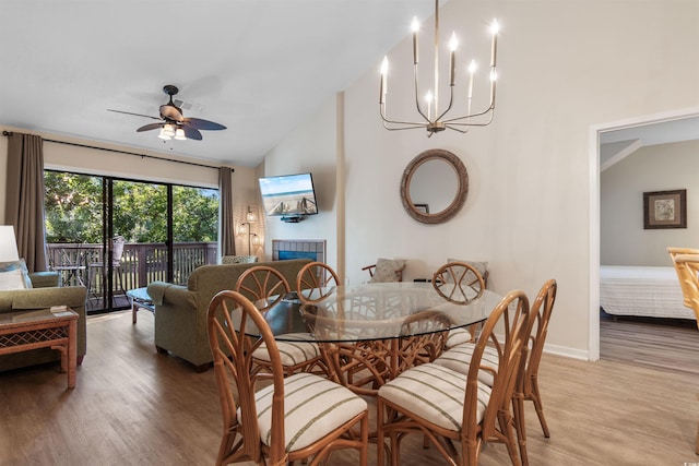 dining space featuring high vaulted ceiling, ceiling fan with notable chandelier, a tile fireplace, and light wood-type flooring