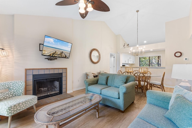 living room featuring a tiled fireplace, high vaulted ceiling, ceiling fan with notable chandelier, and light wood-type flooring