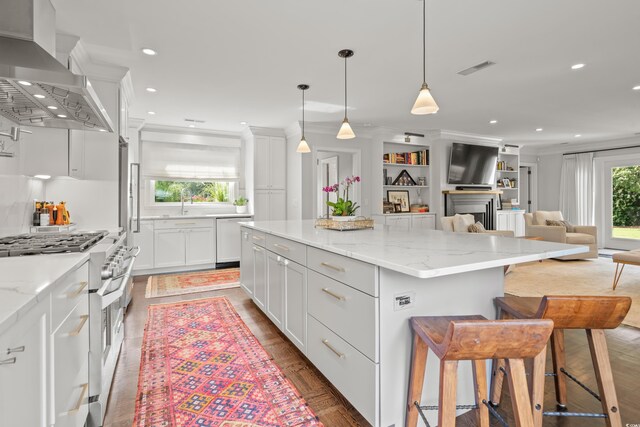 kitchen with light stone counters, double oven range, backsplash, wall chimney range hood, and white cabinets